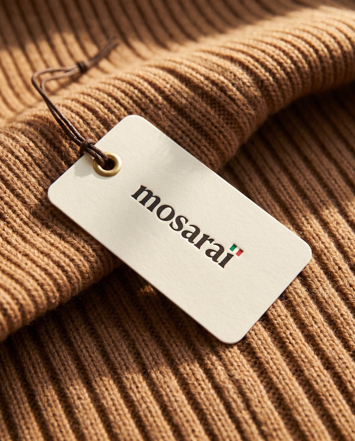 A Mosarai swing tag resting on a caramel ribbed knit